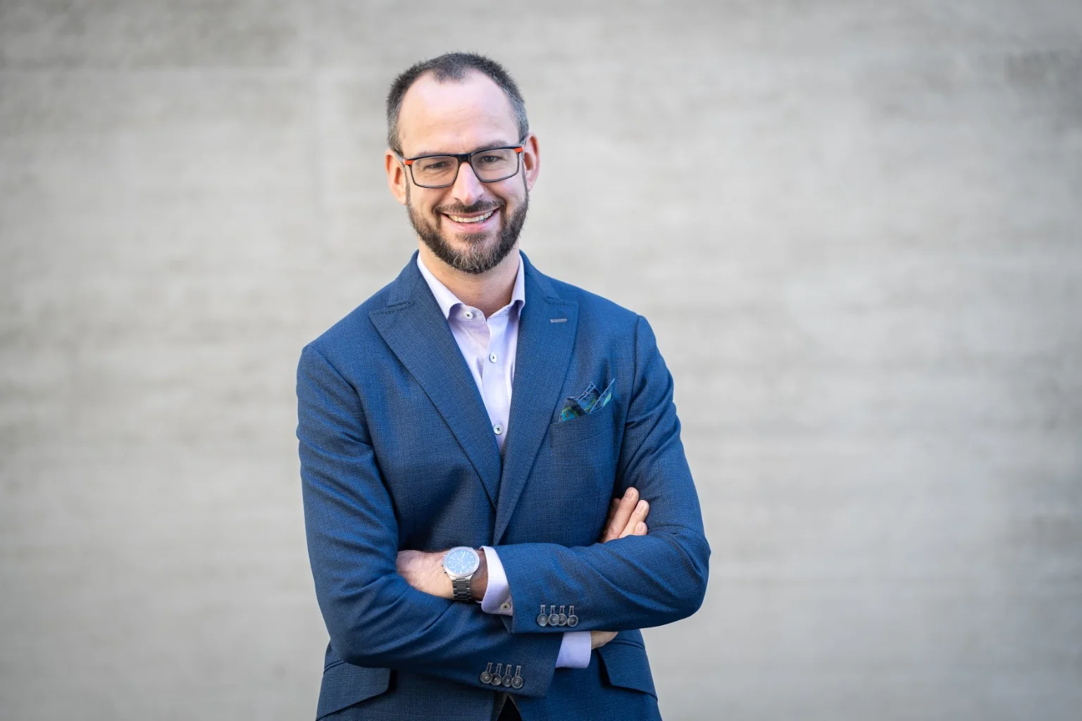 Sascha Hartmann im blauen Sakko vor ruhiger grauer Wand
